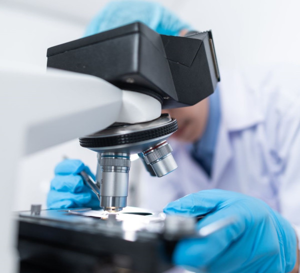 A person wearing a lab coat looking in to a microscope